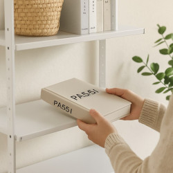 Libro de tapa dura beige con texto negro "PA51" en una estantería con plantas y cesta.