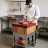 Mesa de preparación de carne con superficie roja, chef cortando carne en un ambiente de cocina profesional.