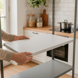 Person placing a white shelf onto a grey metal storage rack in a modern kitchen setting.